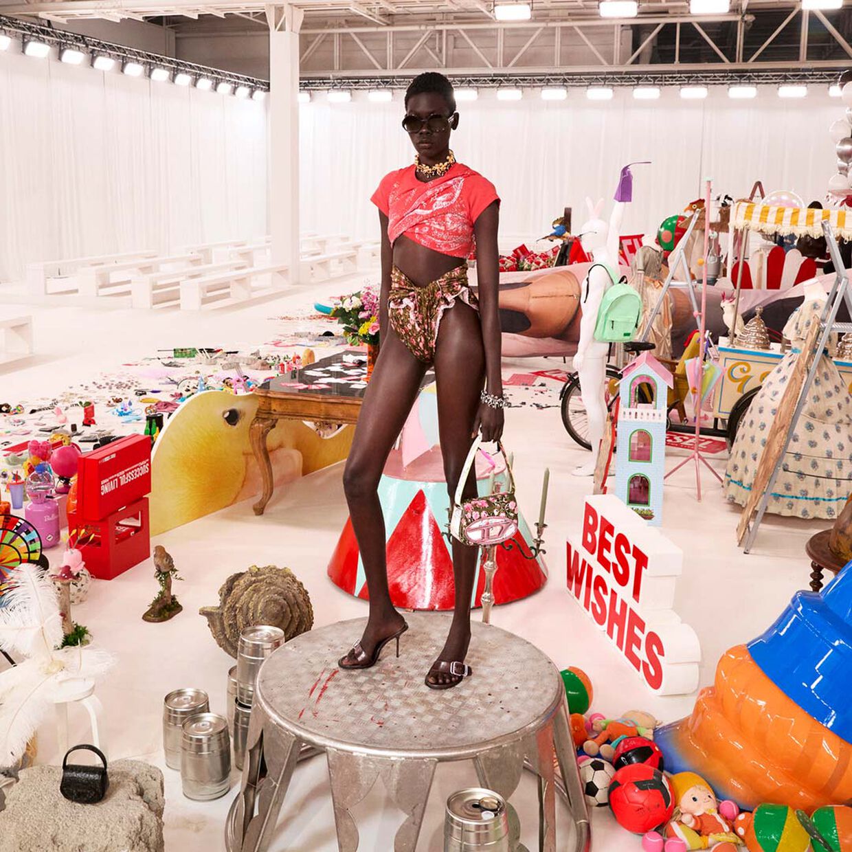 Model wearing denim shorts and a crop-top with the1DR bag, standing in the Fall Winter 2026 Runway Set. 